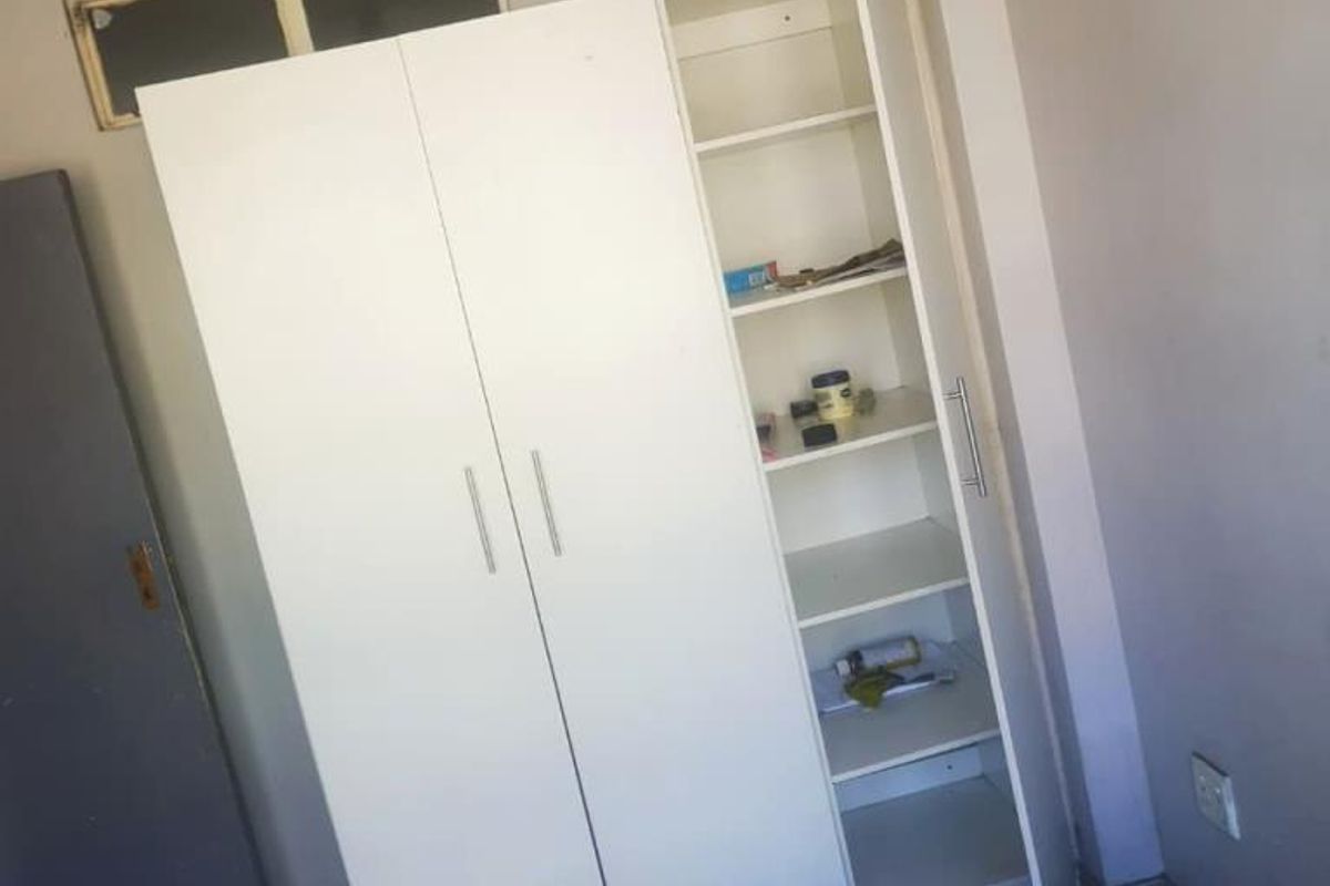 A bedroom featuring tiled flooring and a white built-in wardrobe with integrated shelving.