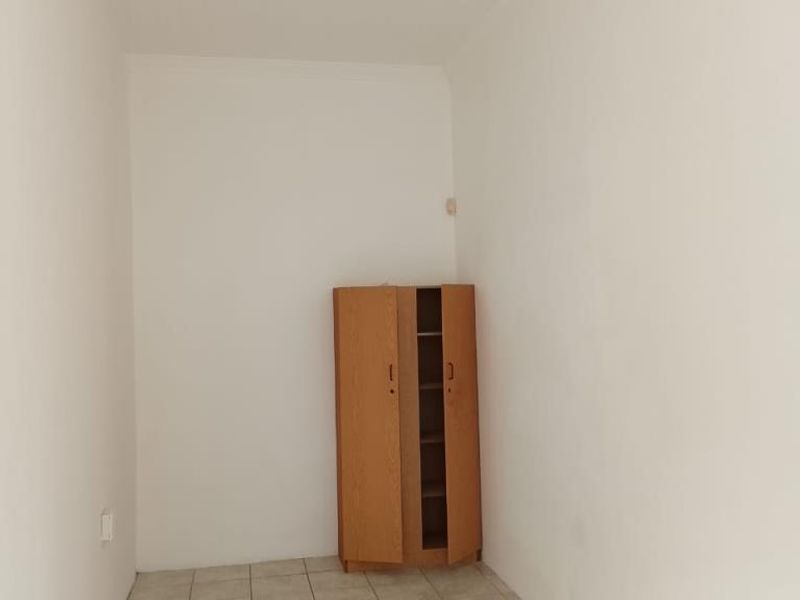 A small, vacant bedroom featuring neutral tiled flooring and white walls, suitable for a compact guest room or home office space.