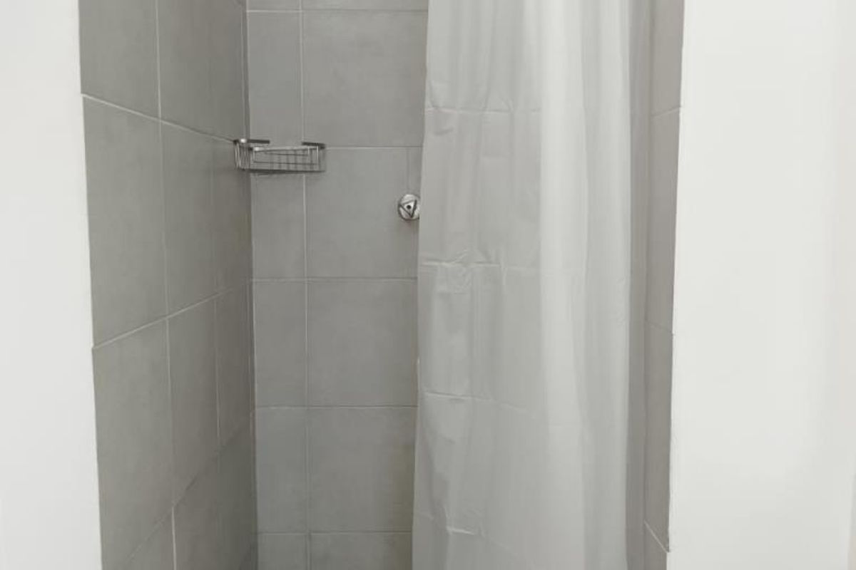 A functional shower stall featuring grey wall tiles, a mosaic tiled floor, and a built-in shower caddy.