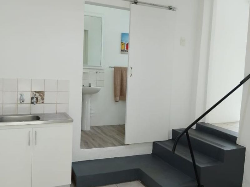 A functional utility area featuring a sink with tiled splashback, a sliding door leading to a bathroom, and a staircase with a handrail.