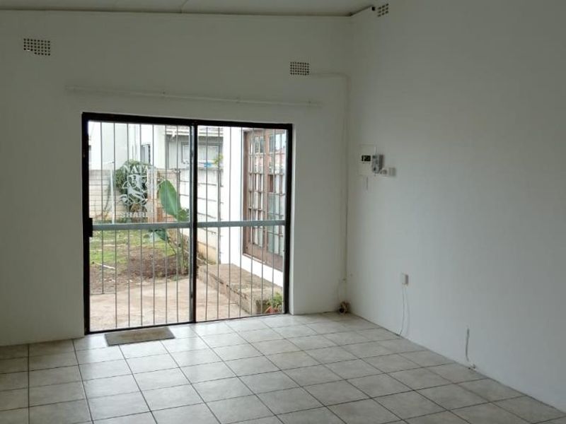 An empty living room featuring tiled flooring and a sliding glass door with a security gate, providing direct access to the exterior.