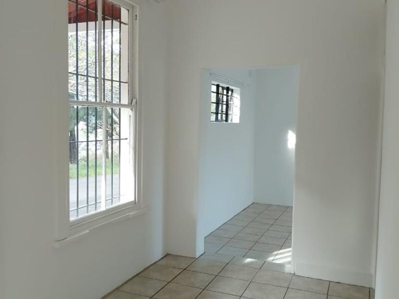 An empty, neutrally painted living area featuring tiled flooring and security bars on the windows, offering a blank canvas for interior design.