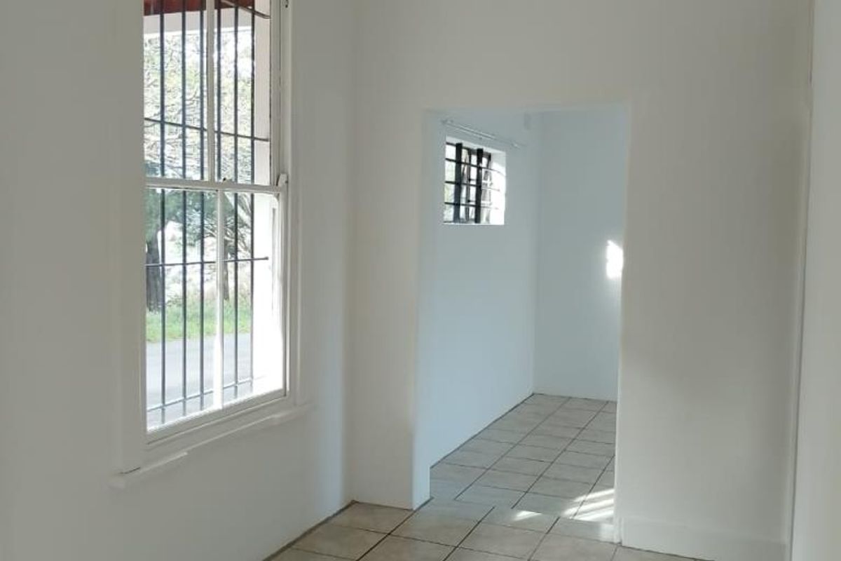 An empty, neutrally painted living area featuring tiled flooring and security bars on the windows, offering a blank canvas for interior design.