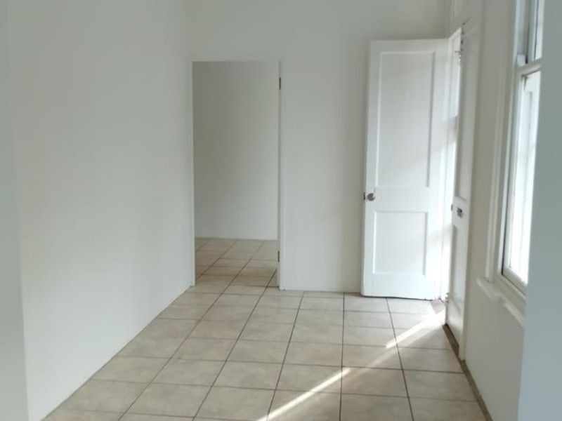 A bright, empty hallway featuring neutral tiled flooring, a classic panel door, and natural light streaming through a side window.