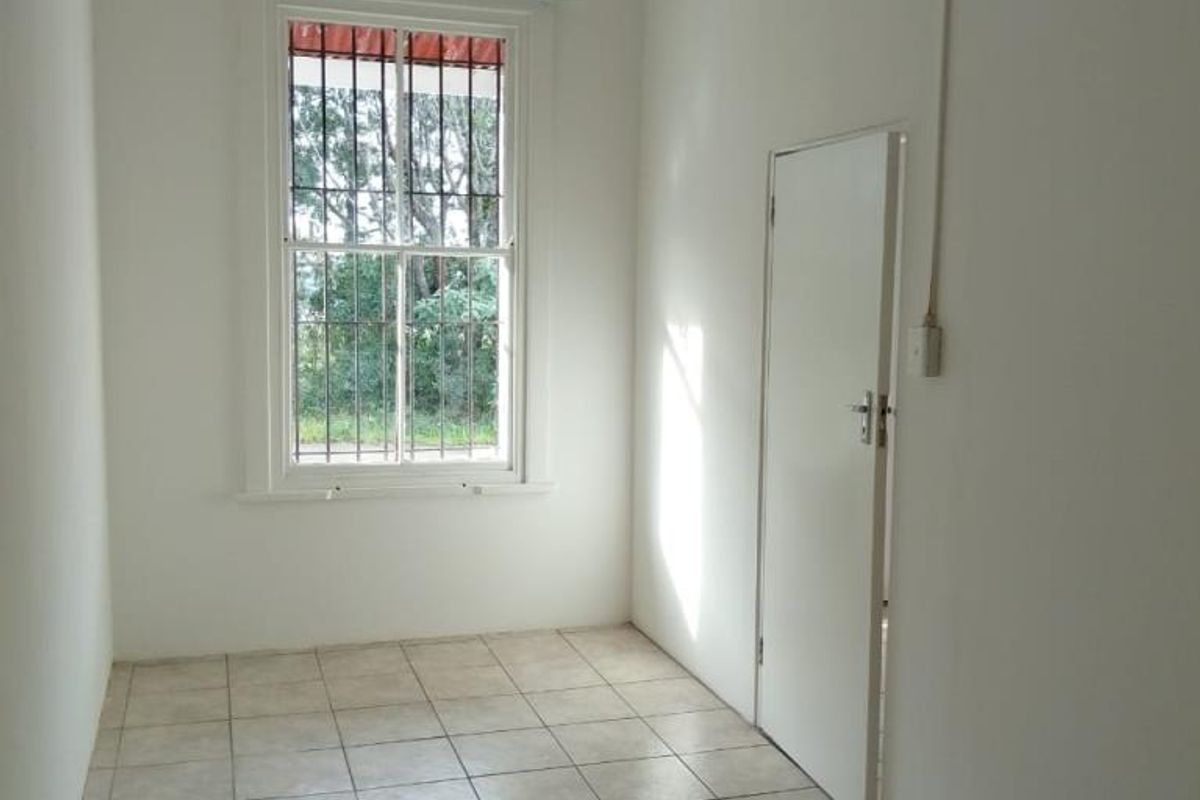 A vacant bedroom featuring neutral white walls, tiled flooring, and a sash window fitted with security bars.