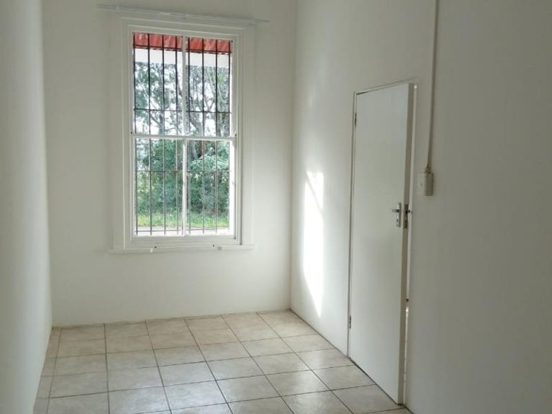 A vacant bedroom featuring neutral white walls, tiled flooring, and a sash window fitted with security bars.