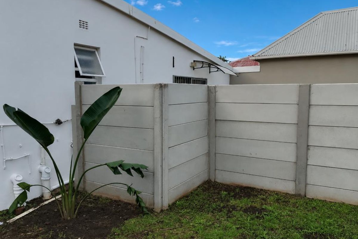 Rear exterior view of the apartment featuring a precast concrete boundary wall, external plumbing fixtures, and a small garden area.