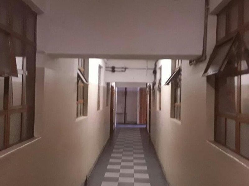 A long, narrow apartment hallway featuring checkered floor tiles and multiple timber-framed windows along the walls.
