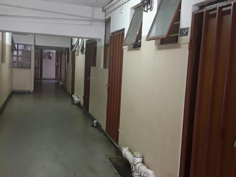 A utilitarian apartment building hallway featuring exposed plumbing, security gates, and multiple unit access doors.