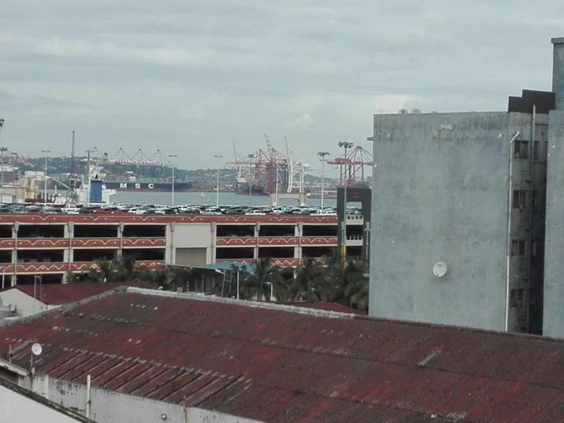 An elevated view overlooking a harbour area with industrial cranes, shipping vessels, and surrounding urban infrastructure.