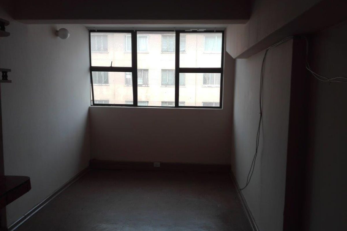 An empty bedroom featuring an aluminium-framed window and basic finishes, requiring cosmetic updates and electrical maintenance.