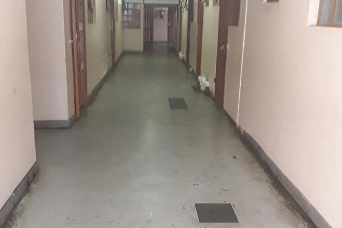 A long apartment building hallway featuring multiple security gates, casement windows, and a fire extinguisher, showing signs of wear and maintenance requirements.
