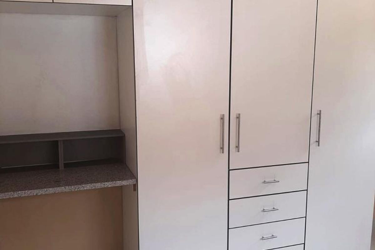 A bedroom featuring white built-in cupboards with integrated drawers and a built-in desk area, finished with neutral floor tiles.