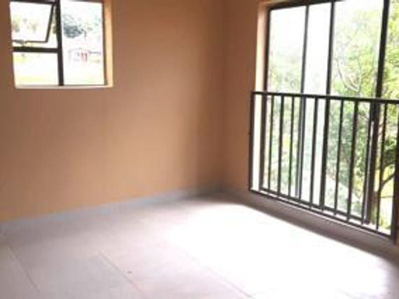An empty bedroom featuring tiled flooring, a sliding glass door leading to a balcony with a metal railing, and a casement window.