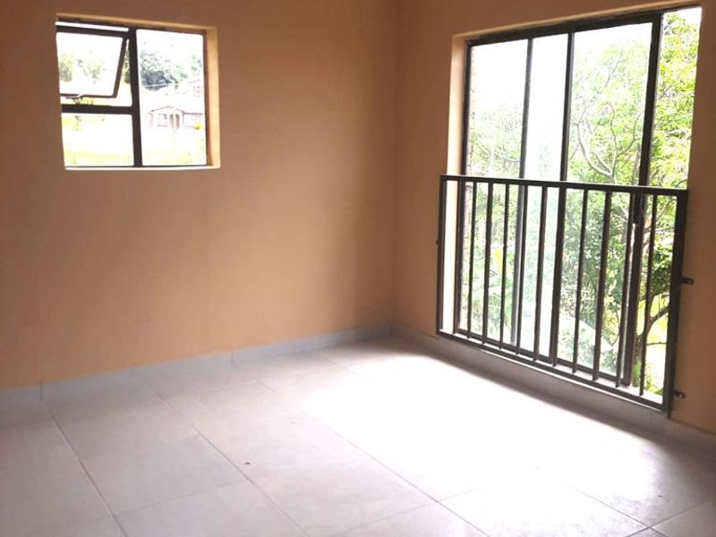 A bright, empty bedroom featuring neutral wall paint, large tiled flooring, and a sliding glass door with a security railing leading to an outdoor view.