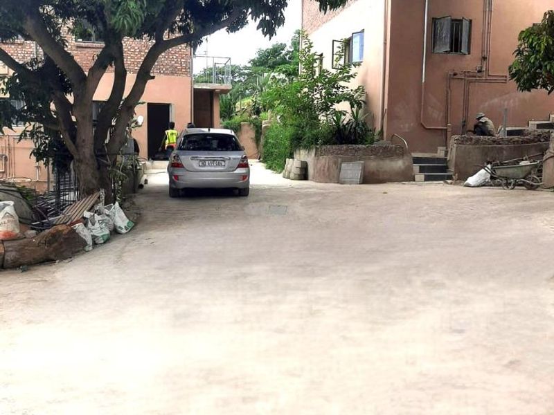 Exterior view of an apartment complex entrance featuring a concrete driveway, masonry building facades, and mature trees.
