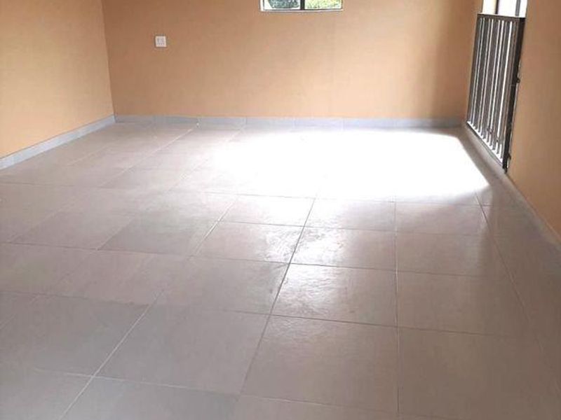 A spacious, empty living area featuring neutral-toned walls, tiled flooring, and a metal security gate leading to an outdoor space.