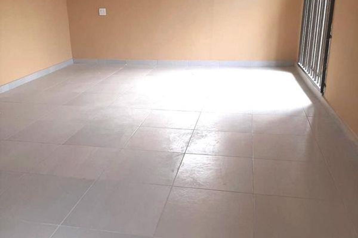 A spacious, empty living area featuring neutral-toned walls, tiled flooring, and a metal security gate leading to an outdoor space.