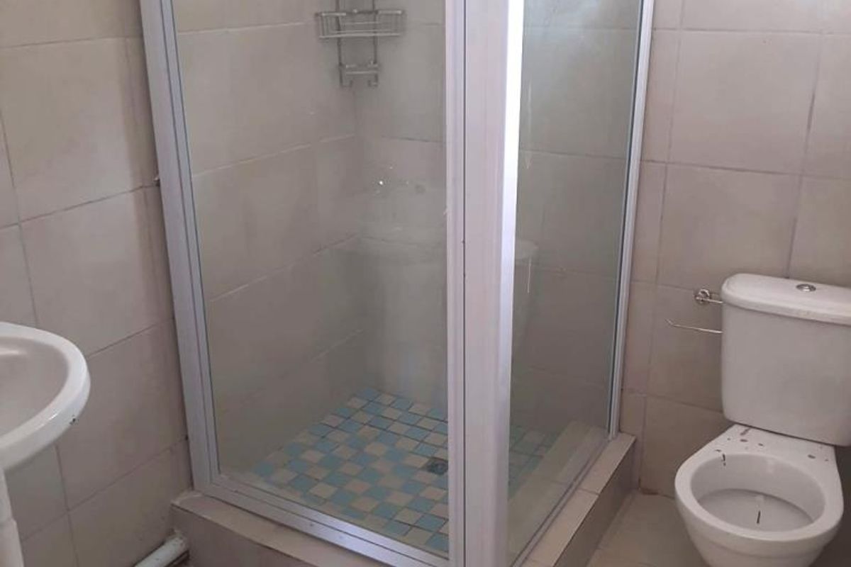 A functional bathroom featuring a shower enclosure, pedestal basin, and toilet with neutral wall and floor tiling.