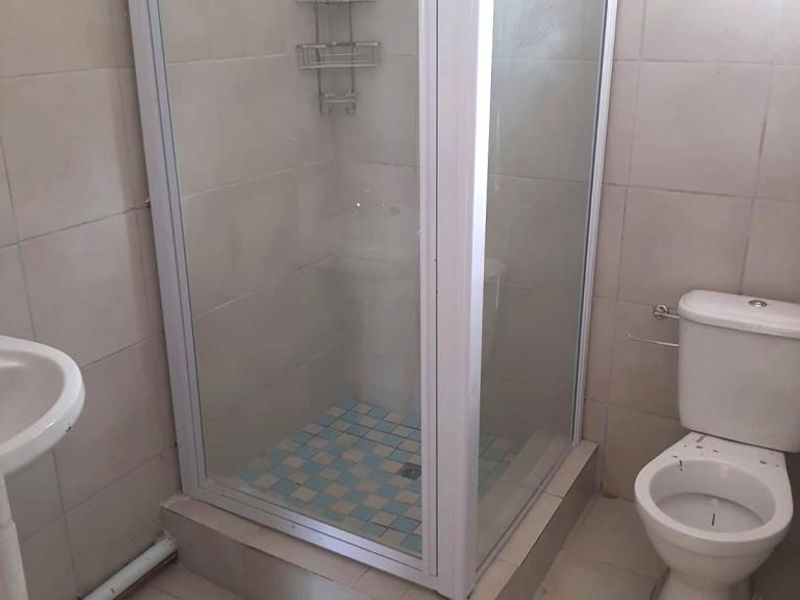 A functional bathroom featuring a shower enclosure, pedestal basin, and toilet with neutral wall and floor tiling.