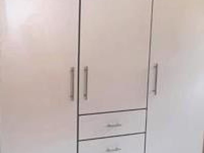 A close-up view of a white built-in wardrobe featuring three doors and three integrated drawers with silver handles.