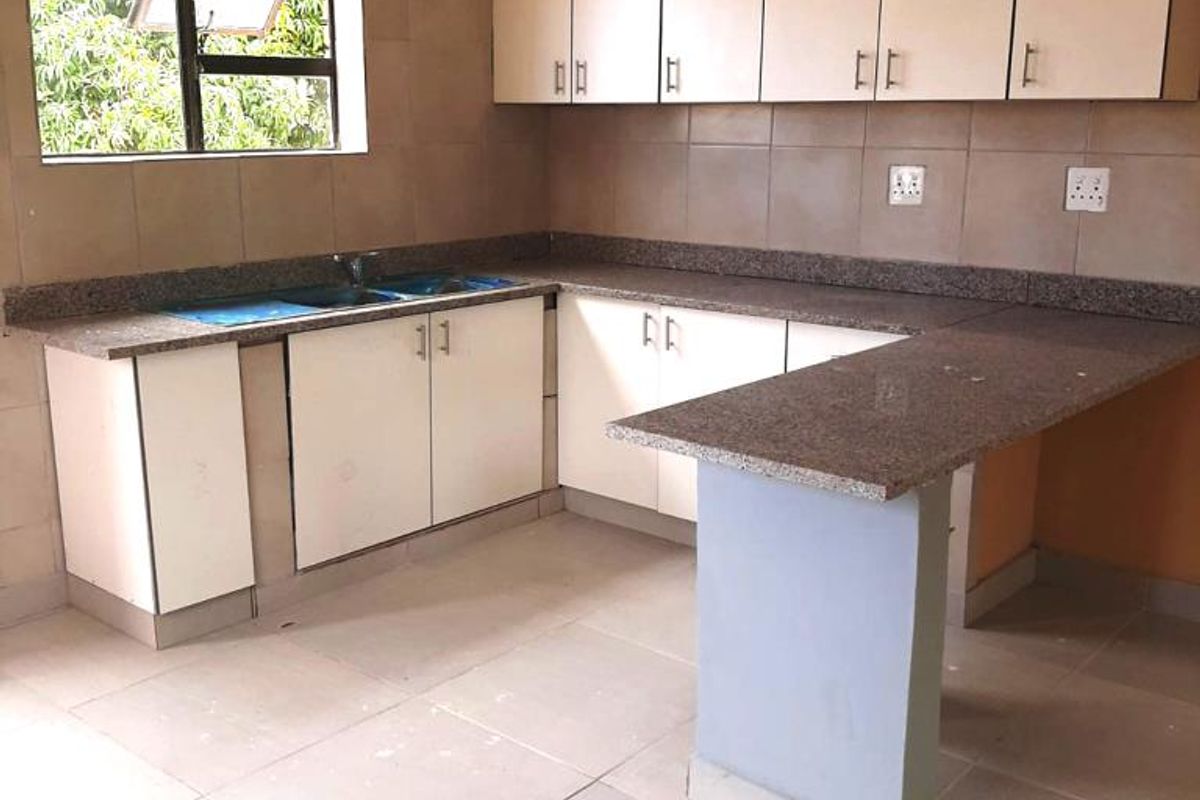 A functional kitchen featuring granite countertops, ample built-in cabinetry, a double bowl sink, and a breakfast bar, finished with neutral wall and floor tiles.