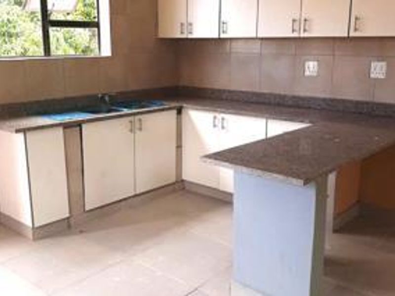 A functional kitchen featuring built-in cabinetry, stone countertops, a breakfast bar, and a double sink with tiled backsplash and flooring.