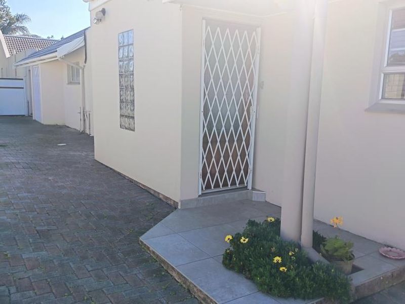 A view of the apartment entrance featuring a paved driveway, tiled porch area, and a security gate.