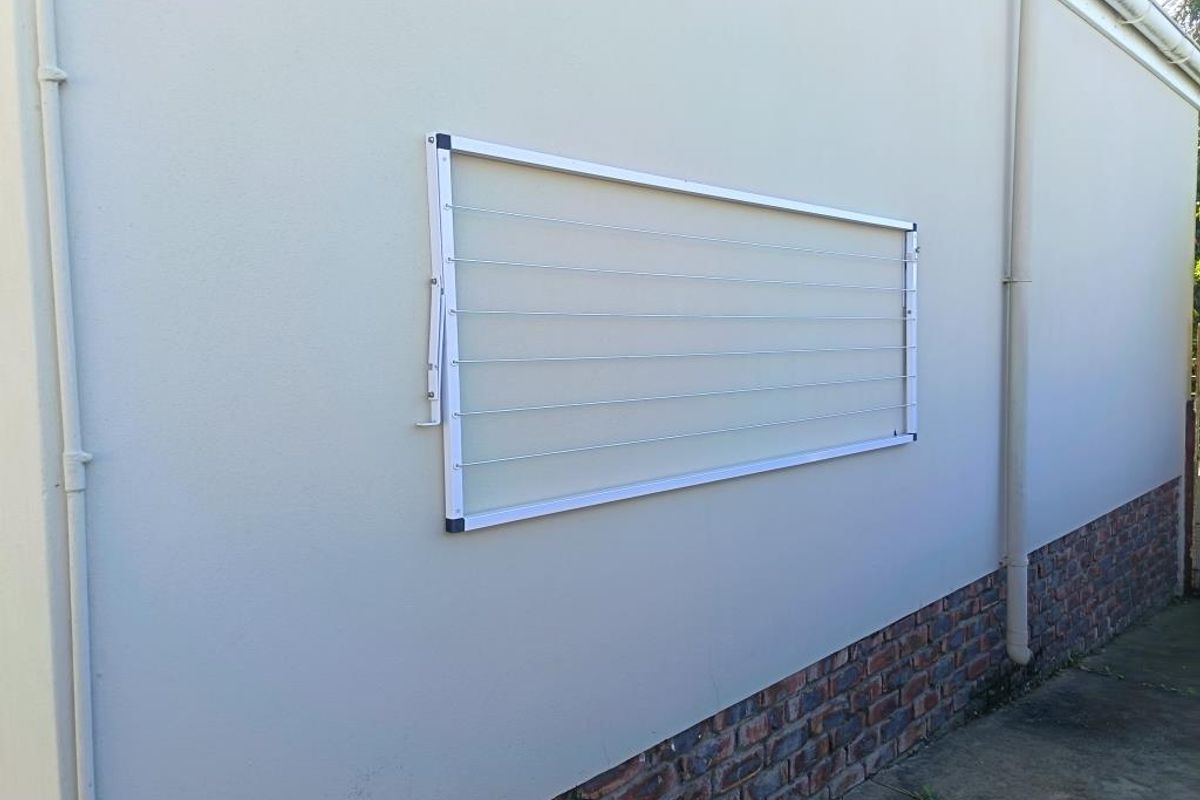 A clean exterior rear wall featuring a wall-mounted clothesline, brick base detailing, and functional drainage downpipes.
