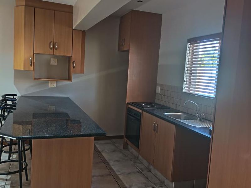 A functional kitchen featuring wooden cabinetry, granite countertops, a built-in oven, and tiled flooring with a breakfast bar area.