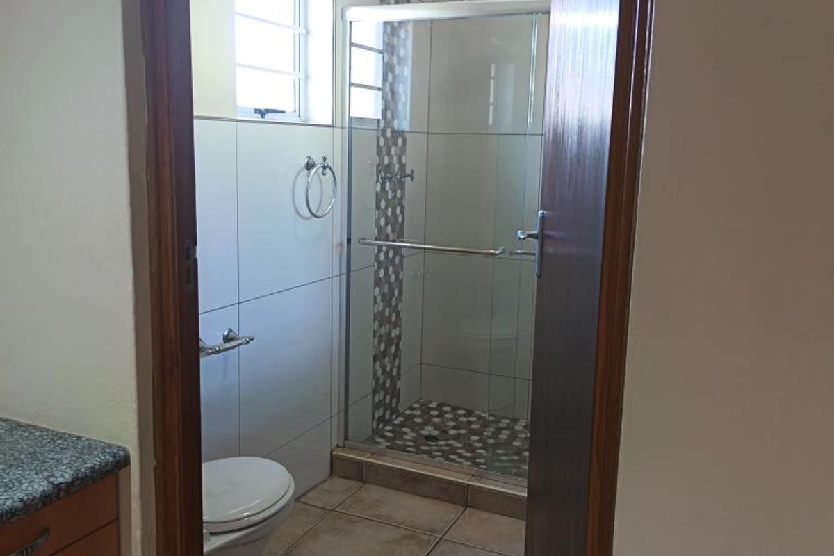 A clean, functional bathroom featuring a glass-enclosed shower, tiled walls with decorative accents, a vanity cabinet with a granite countertop, and tiled flooring.