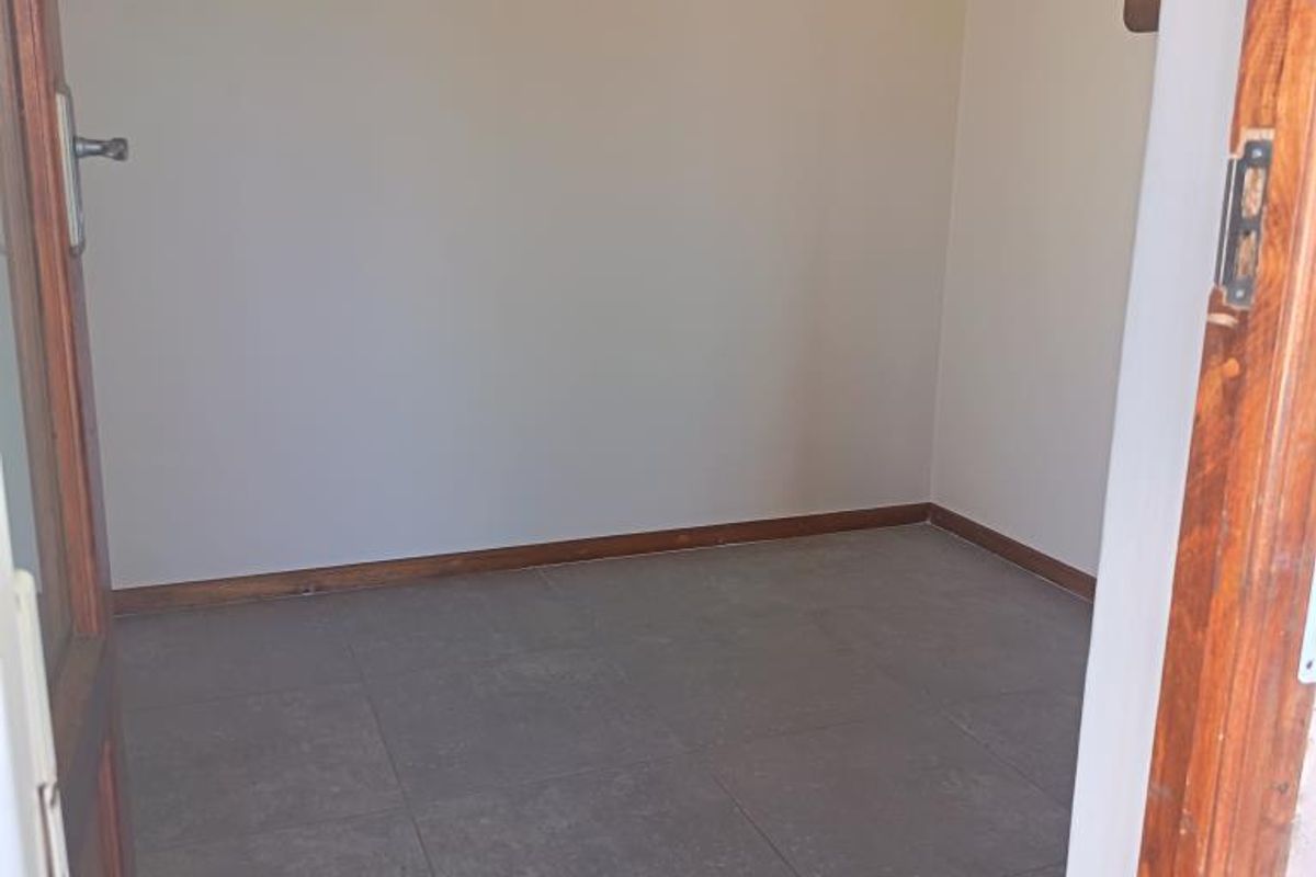 An empty bedroom featuring neutral walls, tiled flooring, and a timber door frame, offering a blank canvas for personalization.