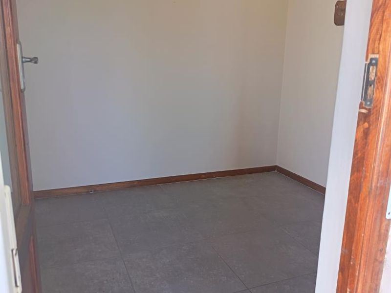 An empty bedroom featuring neutral walls, tiled flooring, and a timber door frame, offering a blank canvas for personalization.