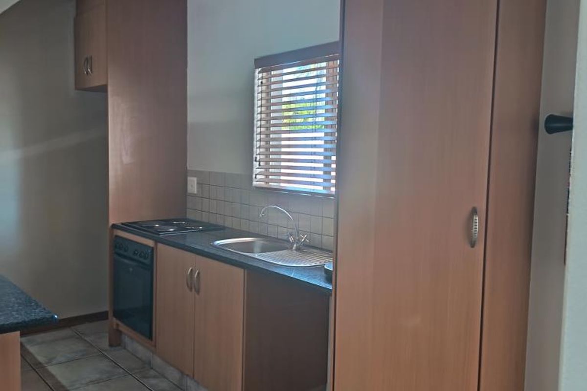 A functional kitchen featuring wood-finish cabinetry, laminate countertops, built-in oven and hob, tiled backsplash, and neutral floor tiles.