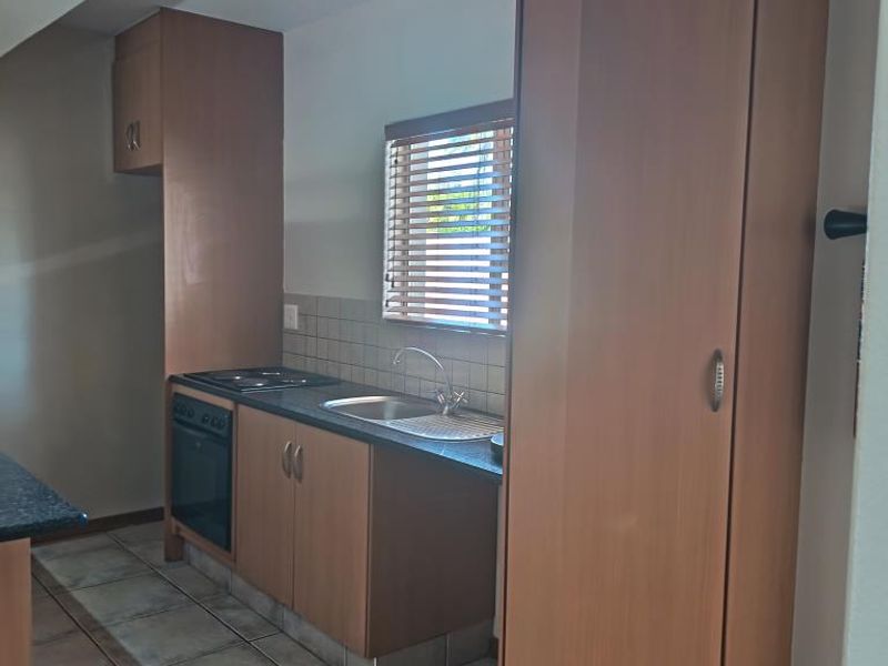A functional kitchen featuring wood-finish cabinetry, laminate countertops, built-in oven and hob, tiled backsplash, and neutral floor tiles.