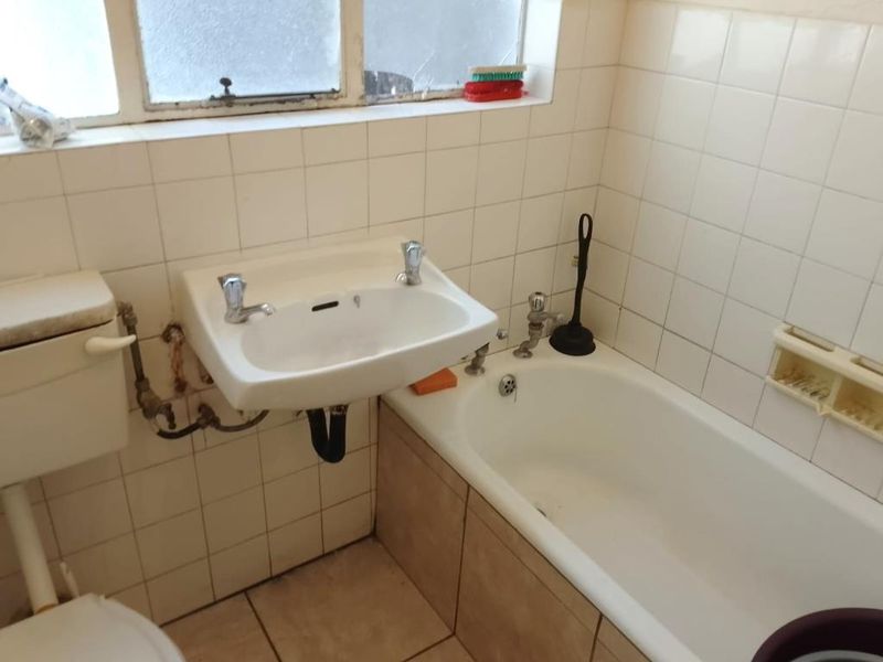 A dated bathroom featuring a wall-mounted basin, bathtub, and toilet, with tiled finishes and visible plumbing requiring maintenance or renovation.
