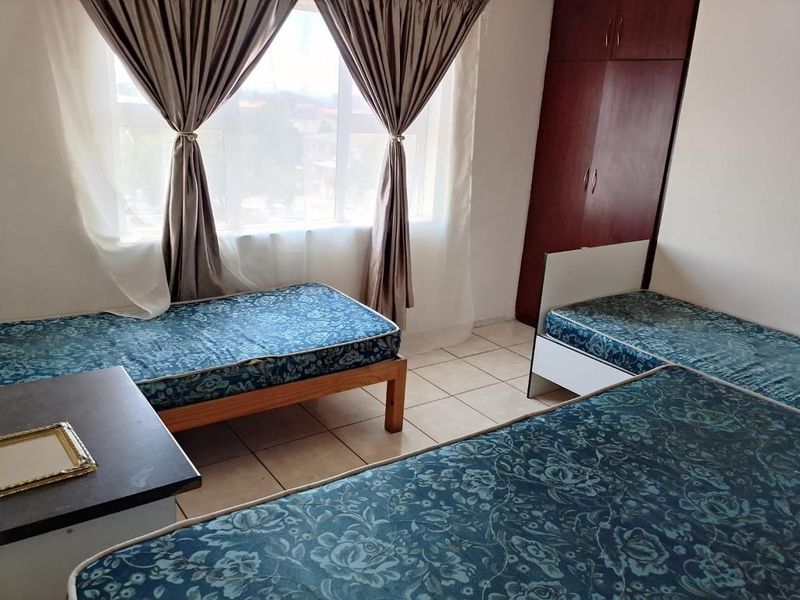 A functional bedroom featuring tiled flooring and a built-in wooden wardrobe, offering a practical layout with natural light from the window.