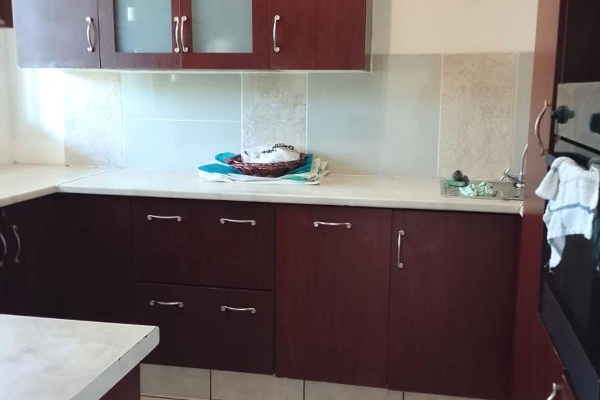 A functional kitchen featuring dark wood cabinetry, light countertops, tiled backsplash, and built-in oven, offering a practical layout for daily meal preparation.