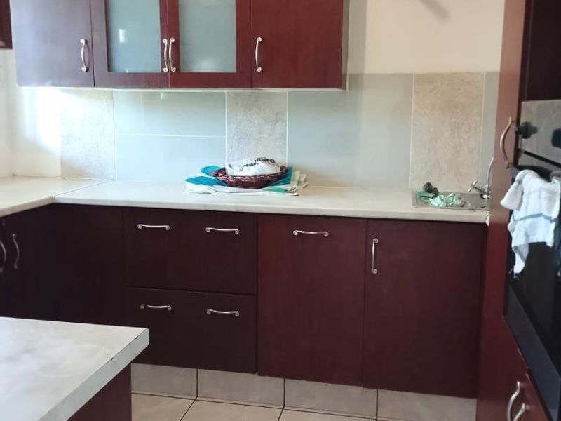 A functional kitchen featuring dark wood cabinetry, light countertops, tiled backsplash, and built-in oven, offering a practical layout for daily meal preparation.