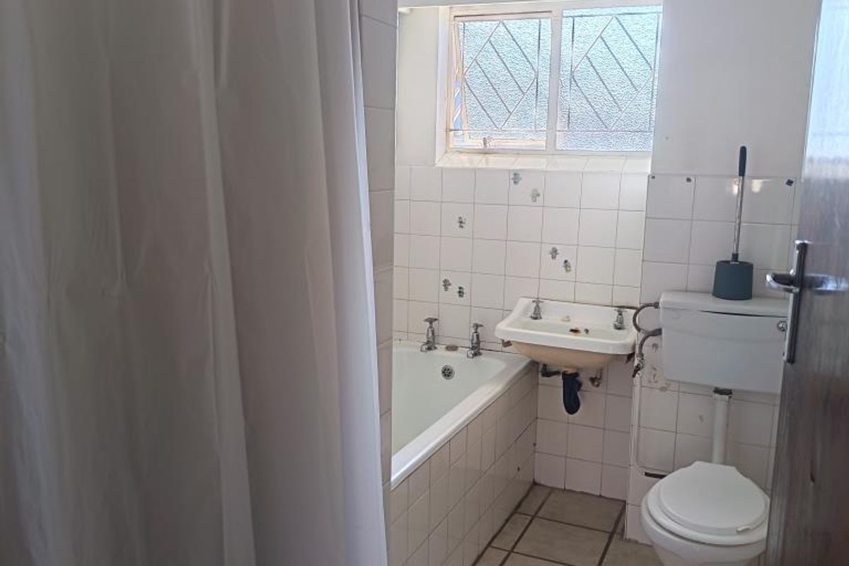 A functional bathroom featuring a bathtub, wall-mounted basin, and toilet with tiled finishes, offering potential for modernization and cosmetic updates.