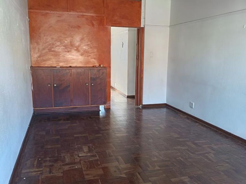 An empty living room featuring original parquet flooring, built-in wooden cabinetry, and neutral wall finishes, offering a blank canvas for renovation.