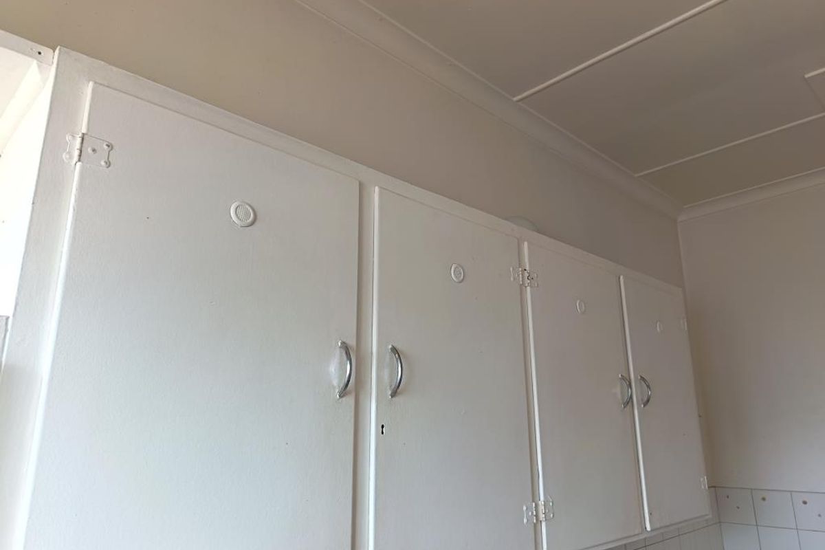 A view of dated kitchen cabinetry with white painted finishes and tiled splashback, offering potential for modern renovation.