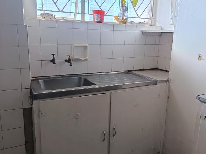 A functional scullery area featuring a stainless steel sink, tiled splashback, and built-in cabinetry, requiring cosmetic updates to improve its overall condition.