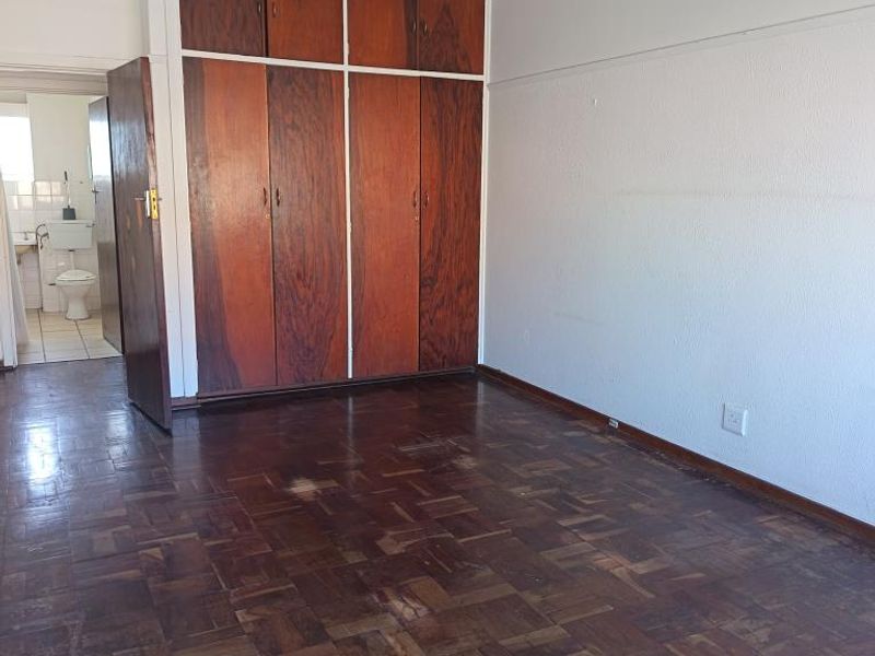 An empty bedroom featuring original parquet flooring and floor-to-ceiling built-in wooden cupboards, with an adjacent view into a bathroom.