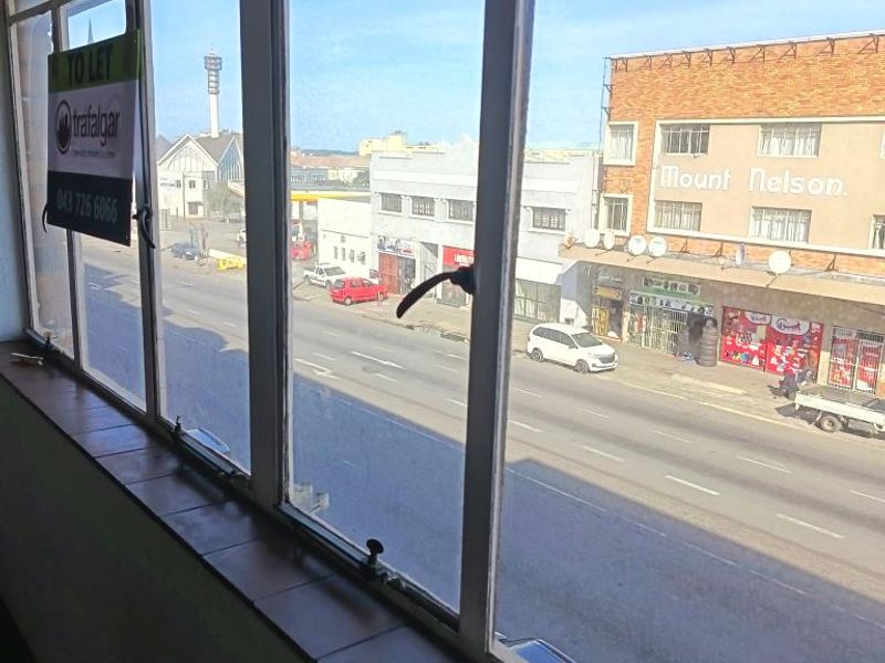 A view from an interior space looking out over a street and neighbouring commercial buildings through large steel-framed windows.