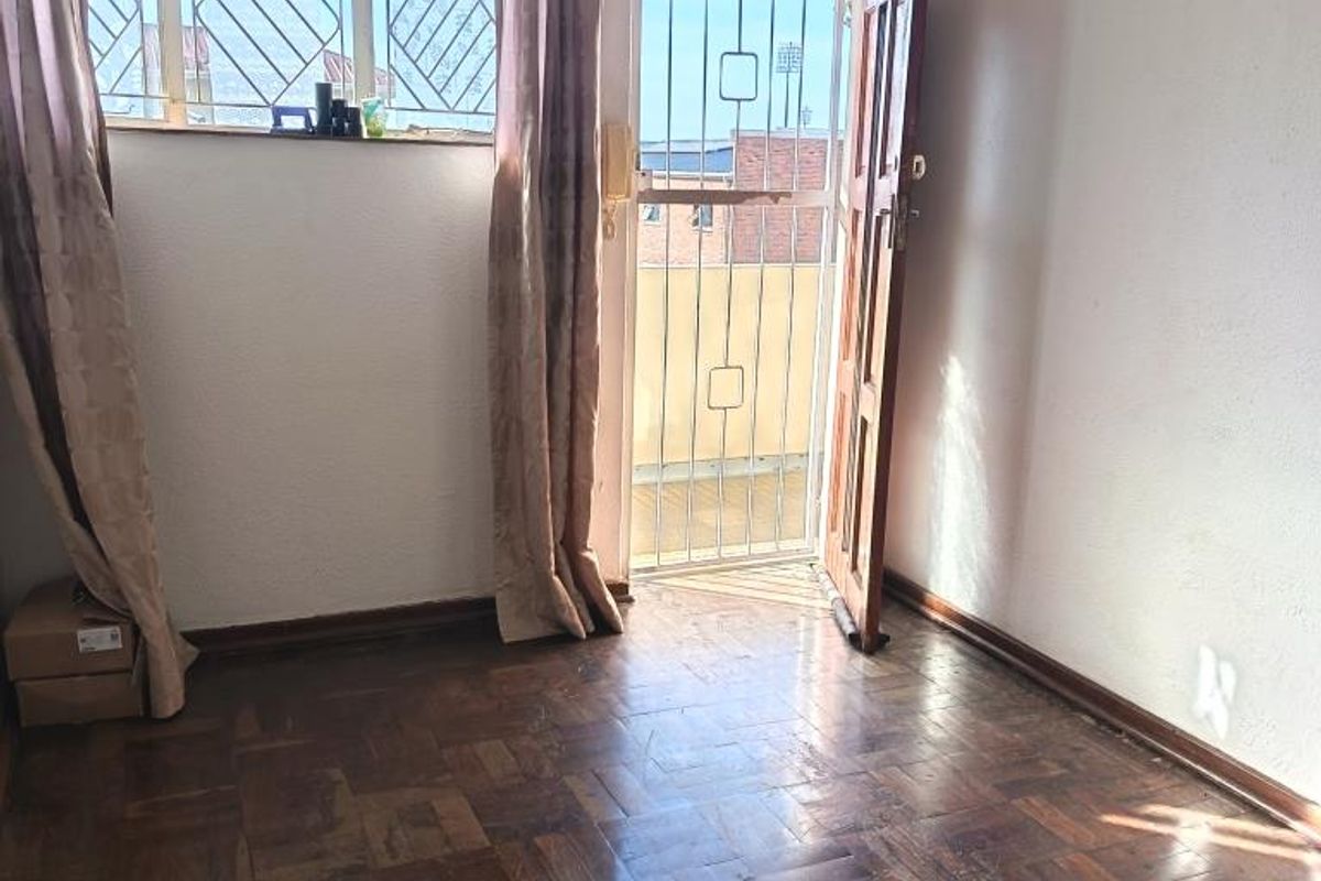 An empty bedroom featuring original parquet flooring, a security gate, and access to an outdoor area, requiring cosmetic updates to the ceiling and floor.