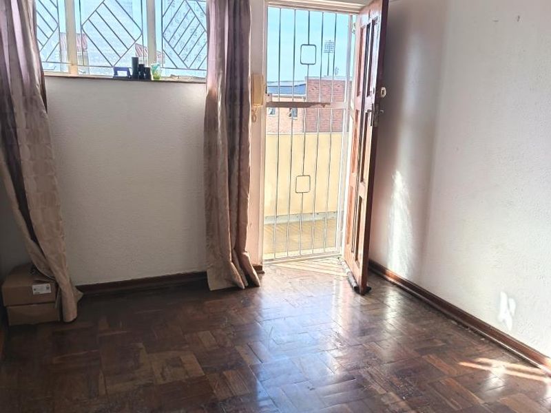 An empty bedroom featuring original parquet flooring, a security gate, and access to an outdoor area, requiring cosmetic updates to the ceiling and floor.