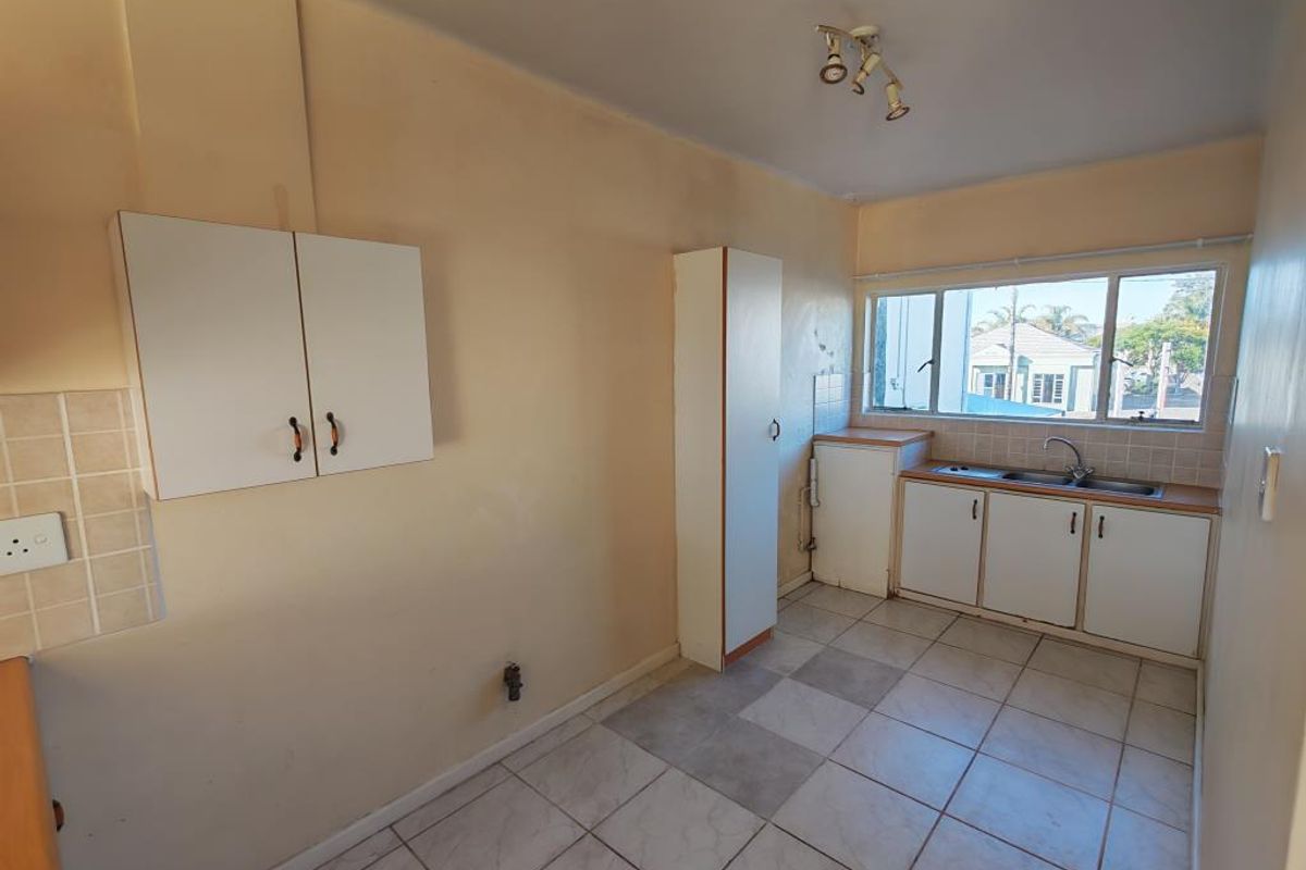 A functional, empty kitchen featuring tiled flooring, built-in cabinetry, and a stainless steel sink, offering a blank canvas for potential renovation and modernization.