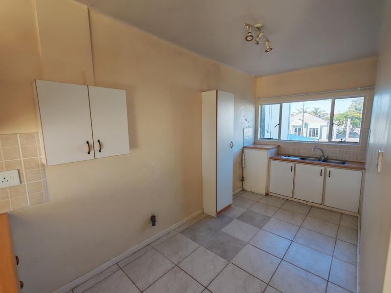 A functional, empty kitchen featuring tiled flooring, built-in cabinetry, and a stainless steel sink, offering a blank canvas for potential renovation and modernization.