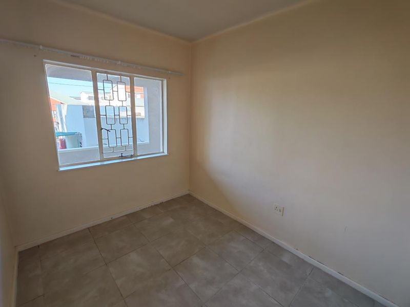 An empty bedroom featuring tiled flooring, neutral walls, and a window fitted with security bars.